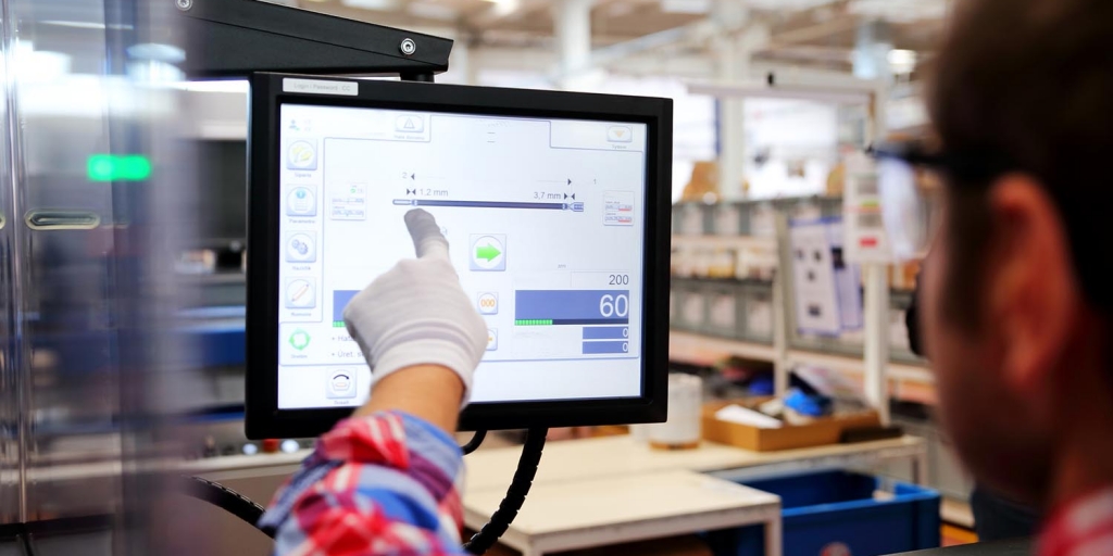 Factory worker a man points at a computer screen showing digital measurements