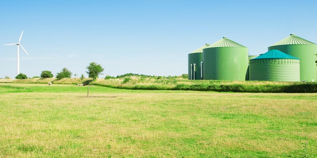 four argicultural silos sit in a green field next to a wind turbine