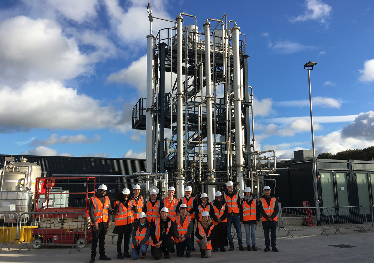 a group of students wearing orange hi vis vests and hard hats stand near a large metal Amine capture plant